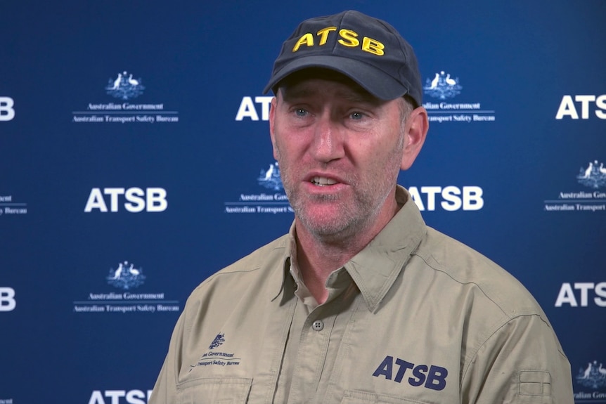 A man wearing a cap and a khaki uniform emblazoned with the letters ATSB stands in a video studio.