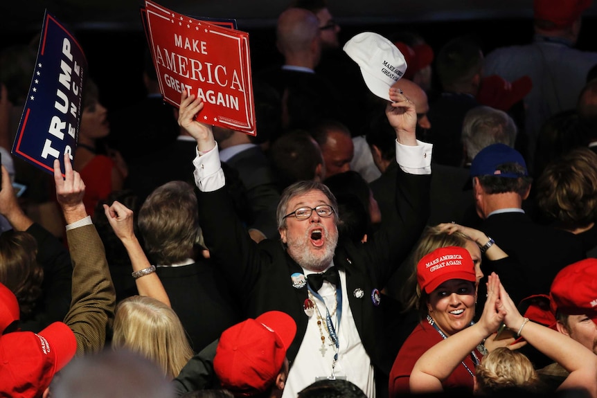 A man holding a Make America Great Again sign celebrates in a crowd of Trump supporters.