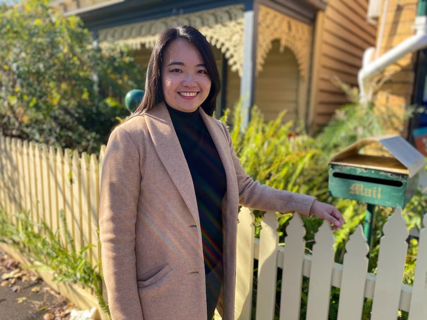 A woman smiles as she rests her hand on a picket fence.