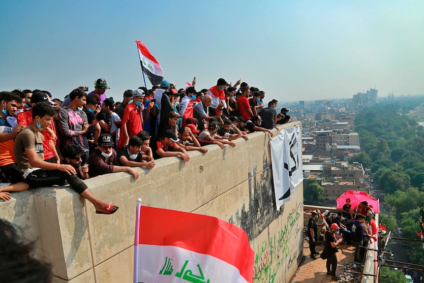 Protesters sit atop the 14-storey building, with flags. A view of the leafy street can be seen and there are blue skies.