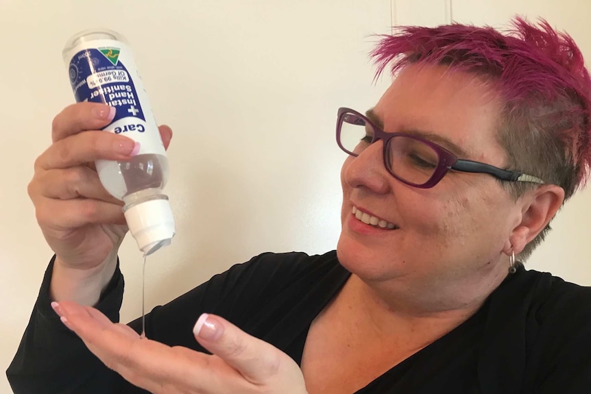 Woman with short pink hair pours hand sanitizer onto her palm with a smile on her face.