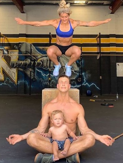 Katelin Van Zyl jumps from a box over her husband and son at a gym.