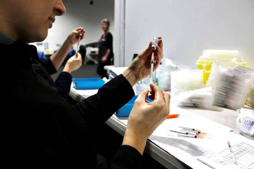 A close-up shot of a woman loading a syringe with the Pfizer COVID-19 vaccine.