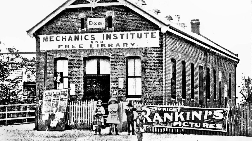 Black and white photo of children outside a brick building, sign reads: Mechanics Institute and Free Library