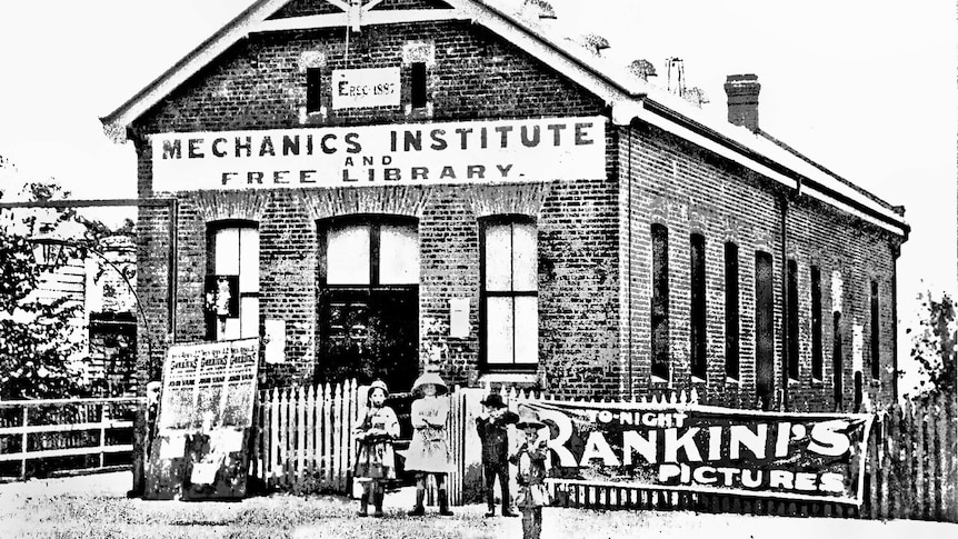 Black and white photo of children outside a brick building, sign reads: Mechanics Institute and Free Library