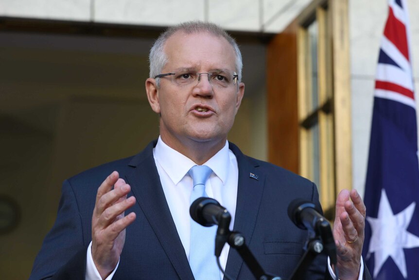 Scott Morrison gestures with his hands while standing behind a lectern.