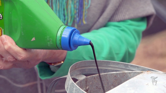 Green bottle with blue sauce lid pouring brown liquid into a metal bucket