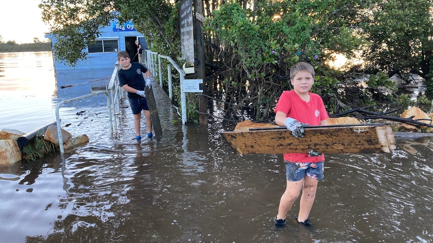 Two young boys carrying flood debris through flood waters from an oyster shed. 