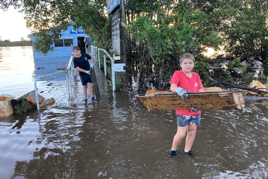 Two young boys carrying flood debris through flood waters from an oyster shed. 