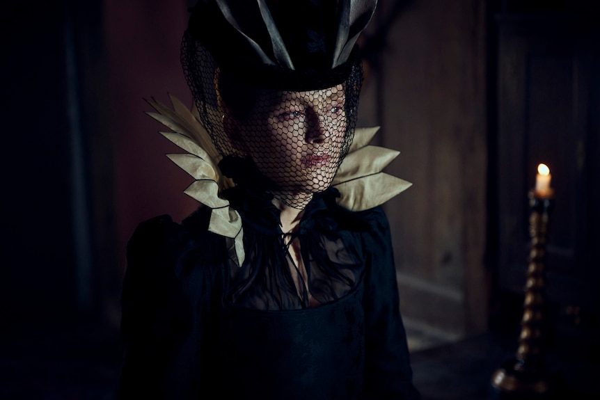 A close up of Moore in costume with a black veil over her face as she looks to the side of the frame with a sombre expression