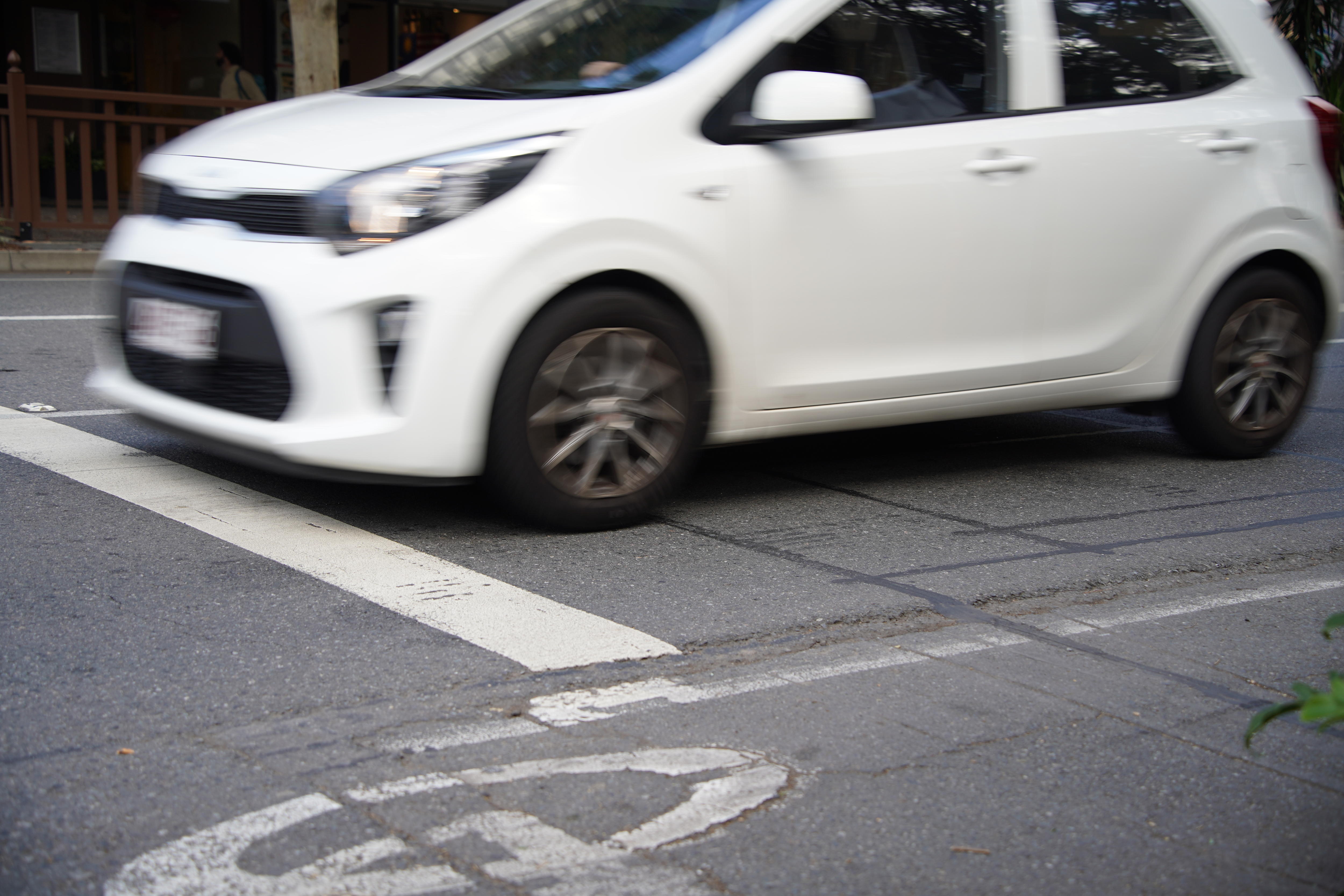 A white car at an intersection with white and black markings on the road.