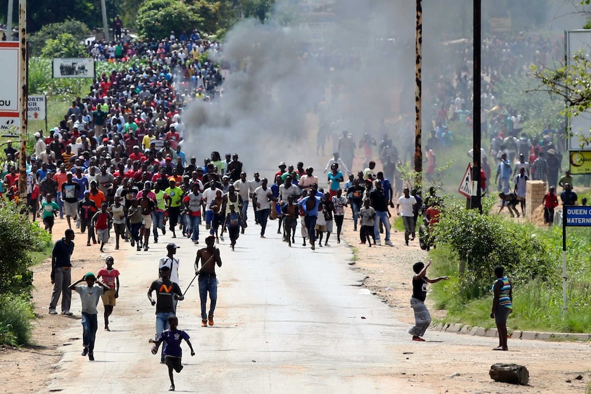 Hundreds of people run from smoke on a street in Harare, Zimbabwe.