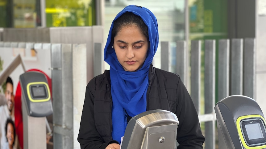 A woman in a hijab scanning a train ticket at a station