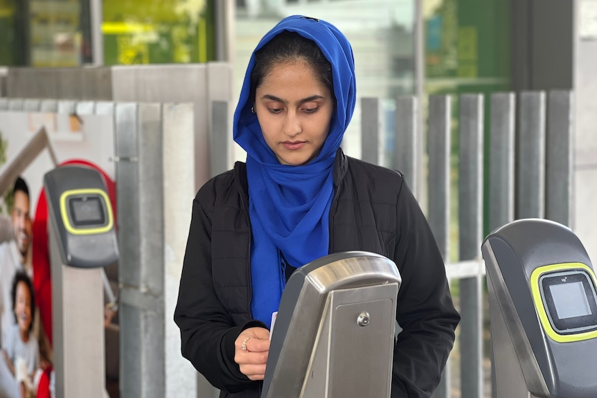 A woman in a hijab scanning a train ticket at a station