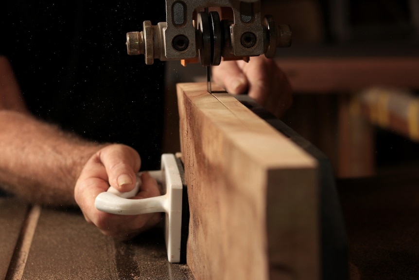 A close-up photo of hands guiding a plank of wood through a band saw.