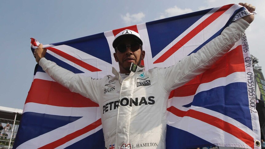 Lewis Hamilton, with helmet off, flies the British flag.