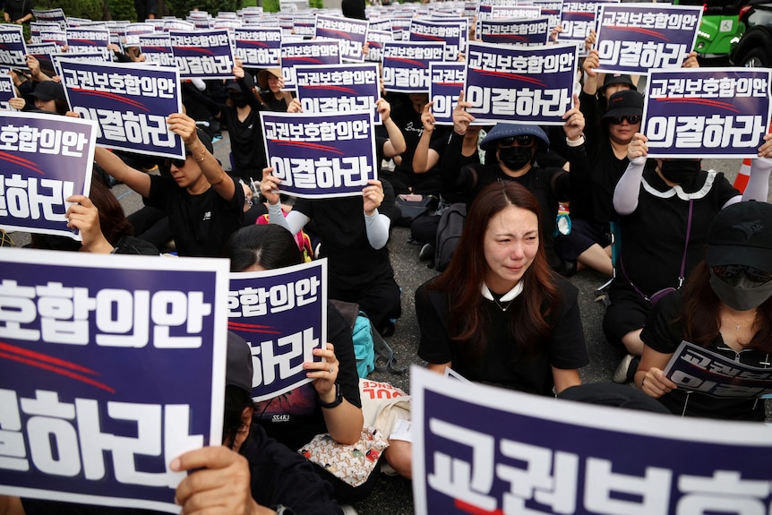 People dressed all in black hold up placards with Korean text. 
