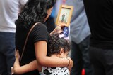 A young girls hugs her mother who is holding a picture of a victim of the September 11 attacks.