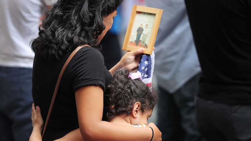 A young girls hugs her mother who is holding a picture of a victim of the September 11 attacks.