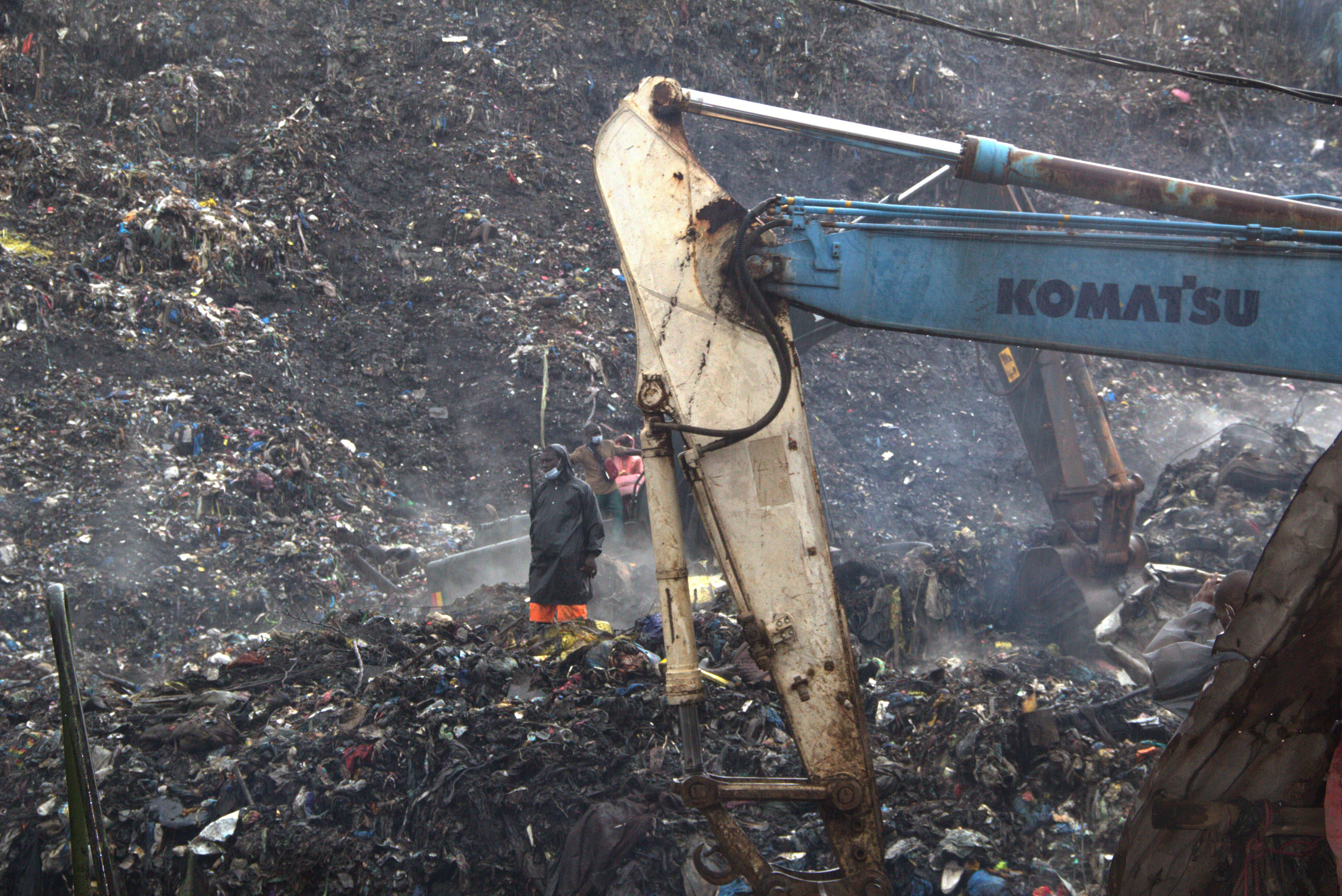 A person stands next to an excavator on a pile of landfill.
