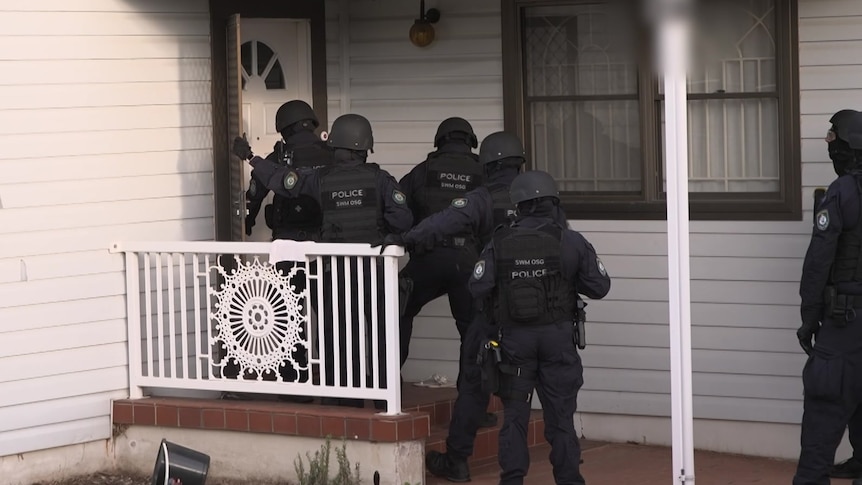 Several police detectives stand outside a house.