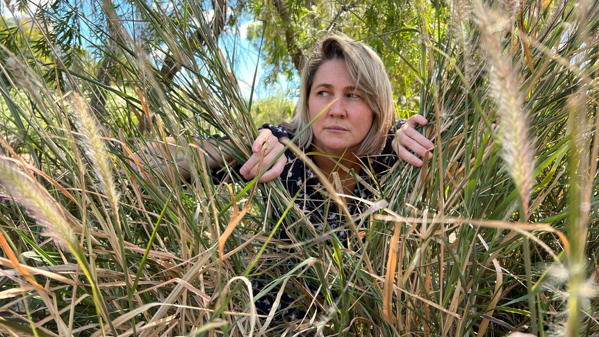 a middle-aged woman hides in a bush looking nervous