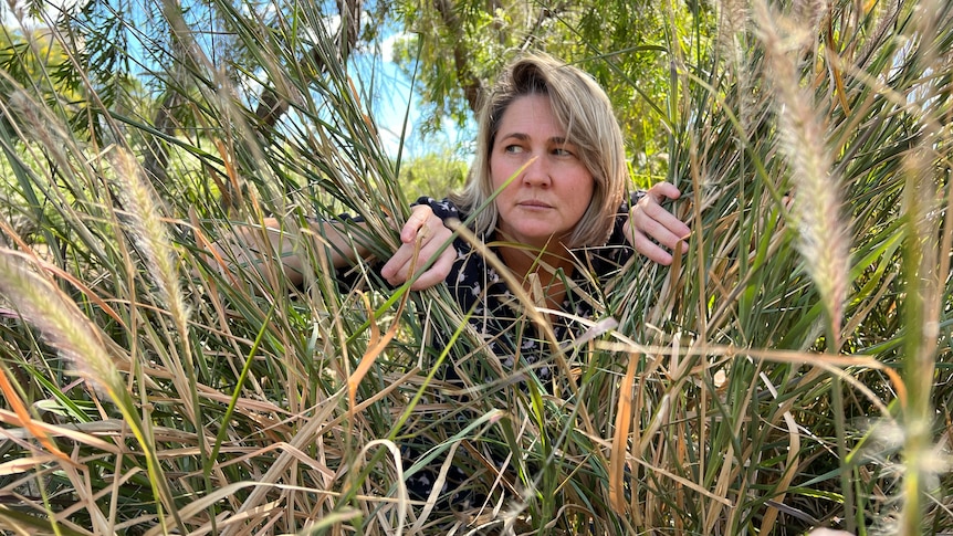 a middle-aged woman hides in a bush looking nervous