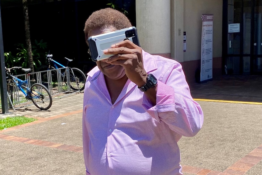 A man shields his face with a phone outside court 