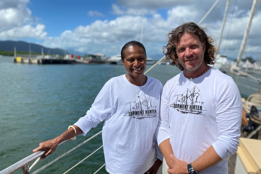 A man and woman stand at the bow of a boat and smile at the camera.