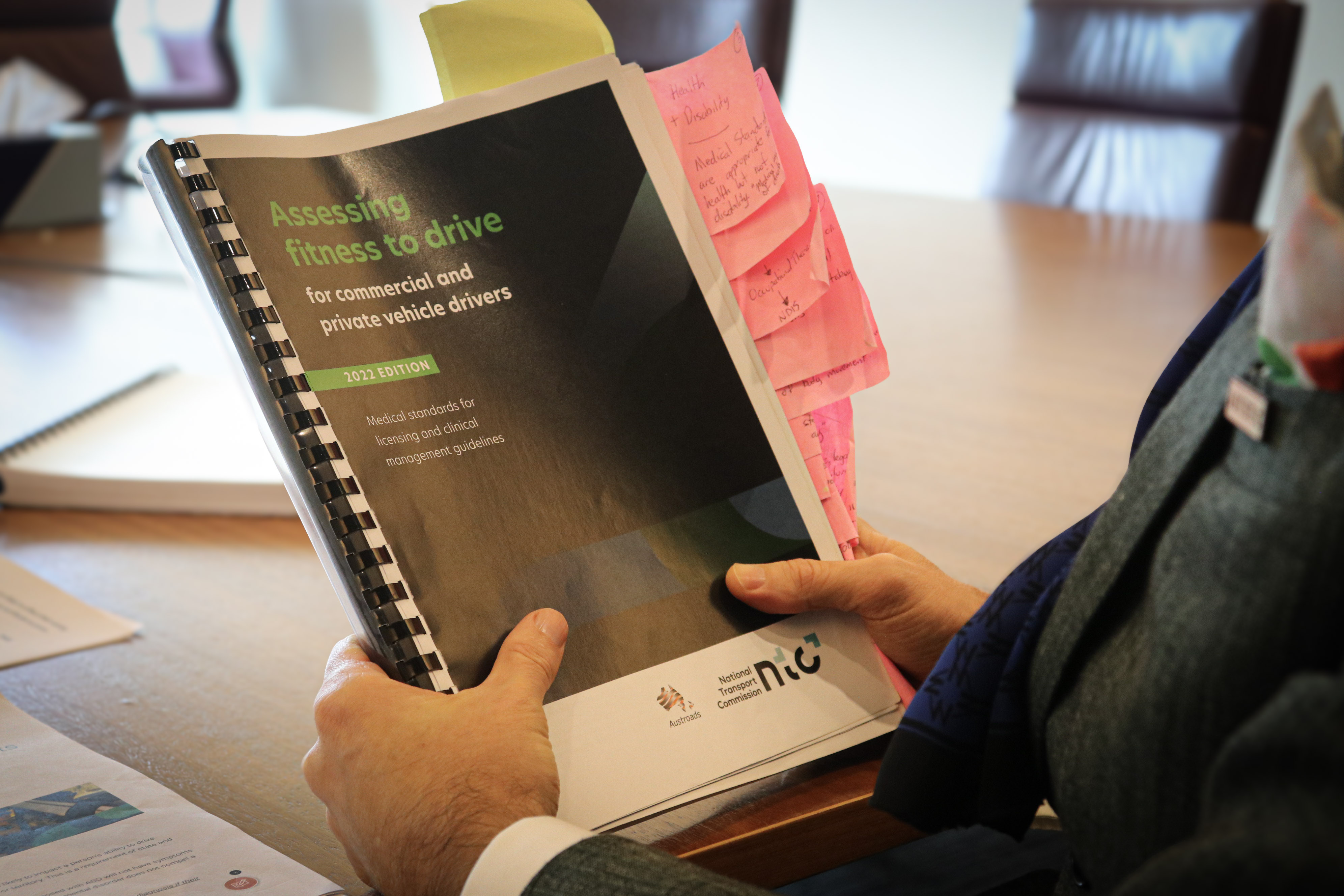 A man holding a booklet that says Assessing Fitness to Drive with pink sticky notes in it.
