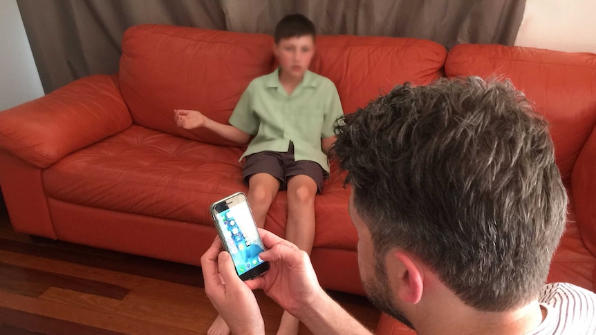 A boy looks annoyed while his father is looking at a mobile phone.