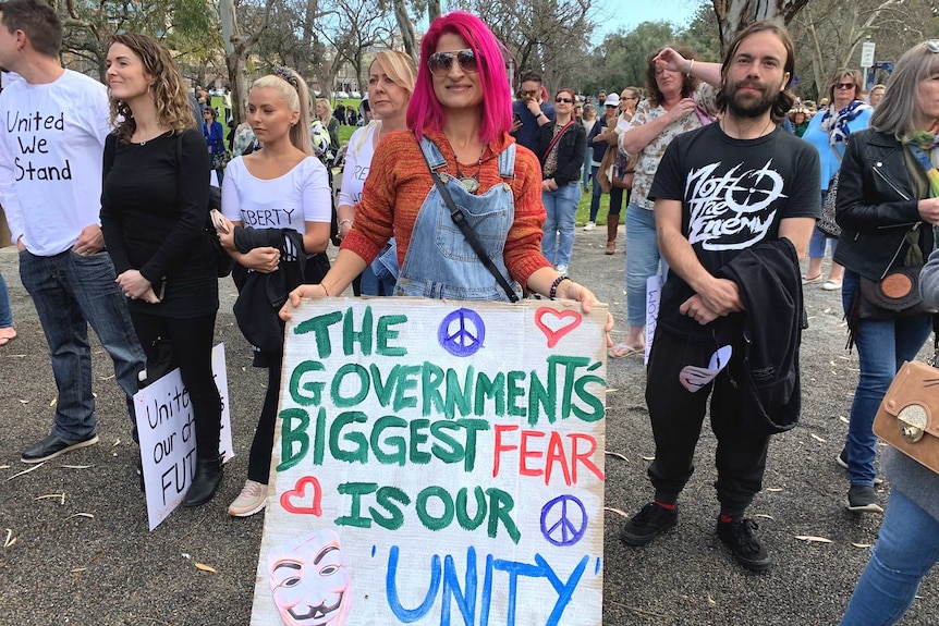 A woman with pink hair holds a large sign with other protesters beside and behind her
