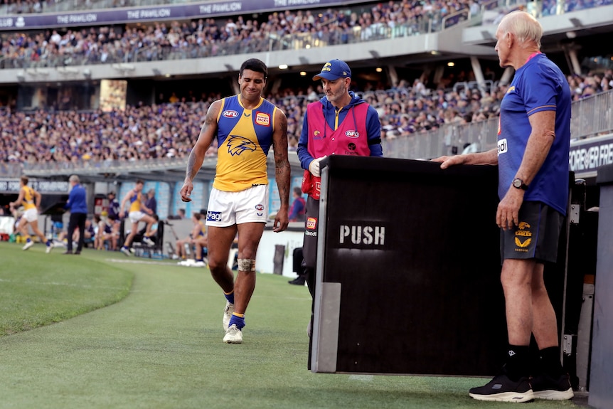 A West Coast player limps around the sideline heading to the rooms after injuring his knee.
