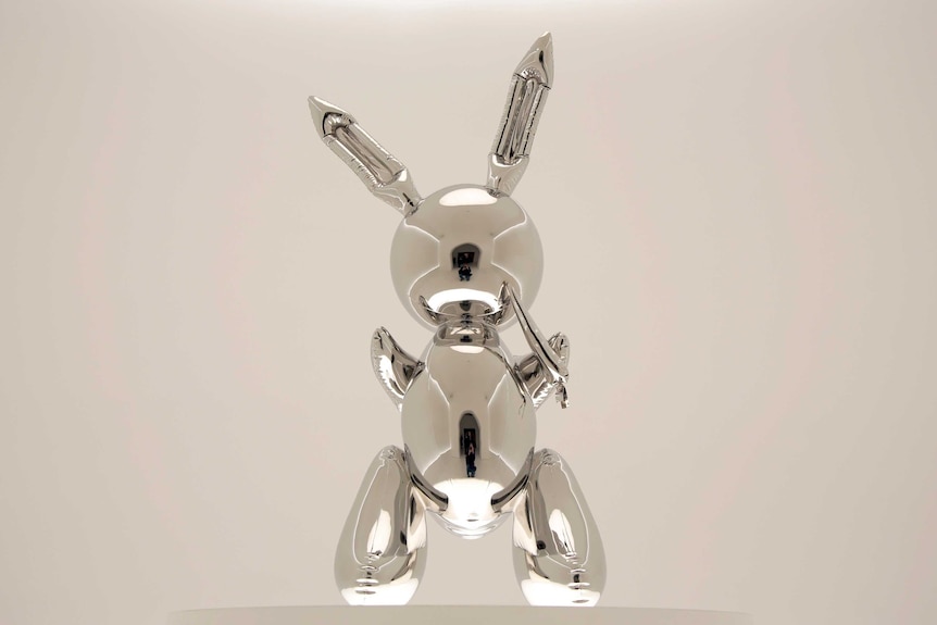 A shiny, faceless oversized rabbit, clutching a carrot sculpture by Jeff Koons.