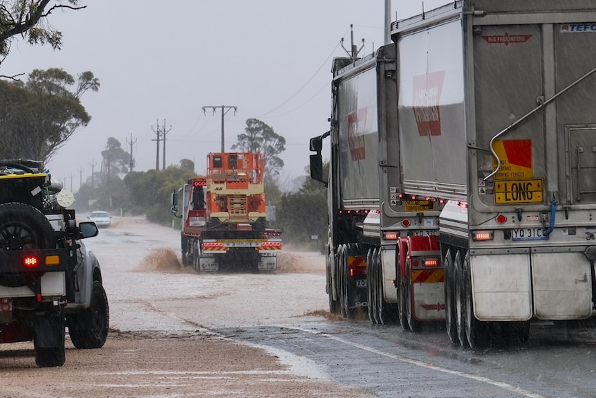 Trucks pass through floodwater on a road.