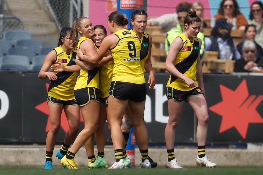 A Richmond AFLW player grins as she gets hugged by teammates after kicking a goal.