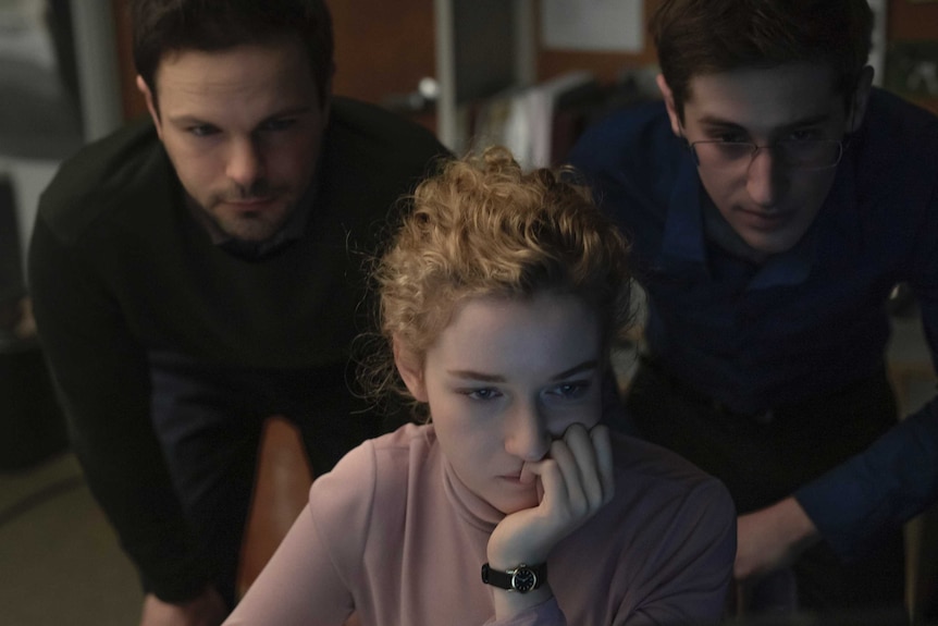 A still from the film The Assistant with three assistants, one female and two male, huddled over a computer