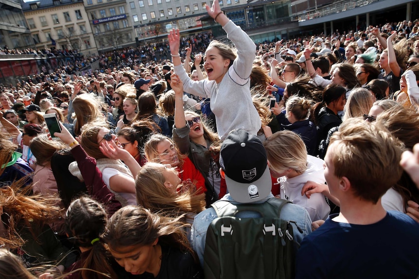 A girl perched on someone's shoulders yells with her arms held above her head