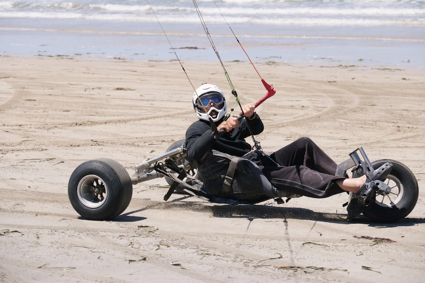 Man in helmet in three-wheel buggy being pulled by lines.