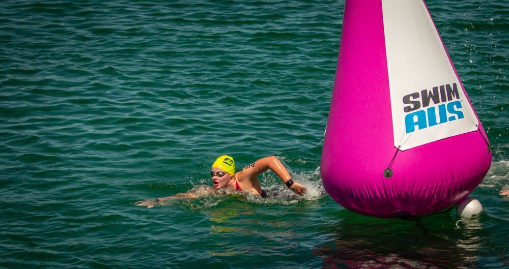 A swimmer in a yellow cap goes around a large pink buoy floating in open water.