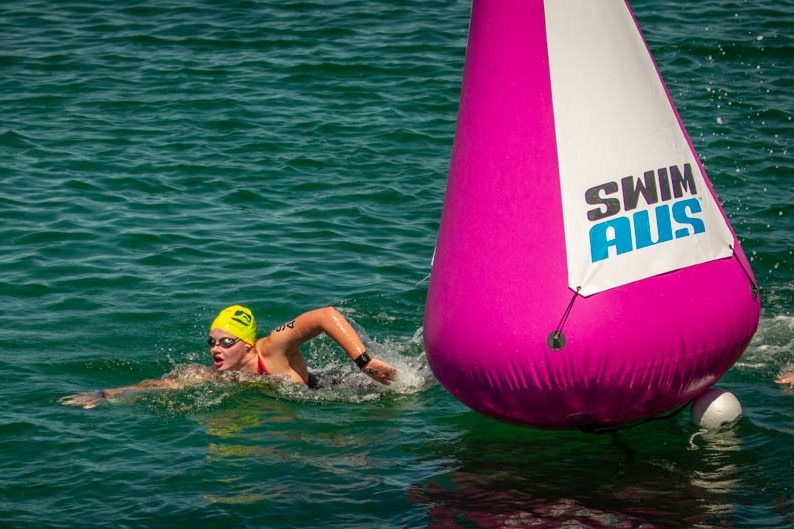 A swimmer in a yellow cap goes around a large pink buoy floating in open water.