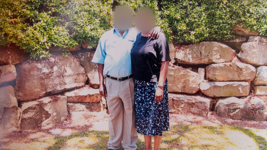 A man and a woman stand next to each other in a family photograph, with their faces blurred.