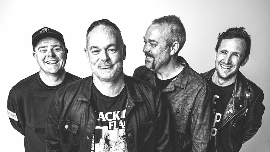 Four men grinning at the camera. They wear jackets and t-shirts.