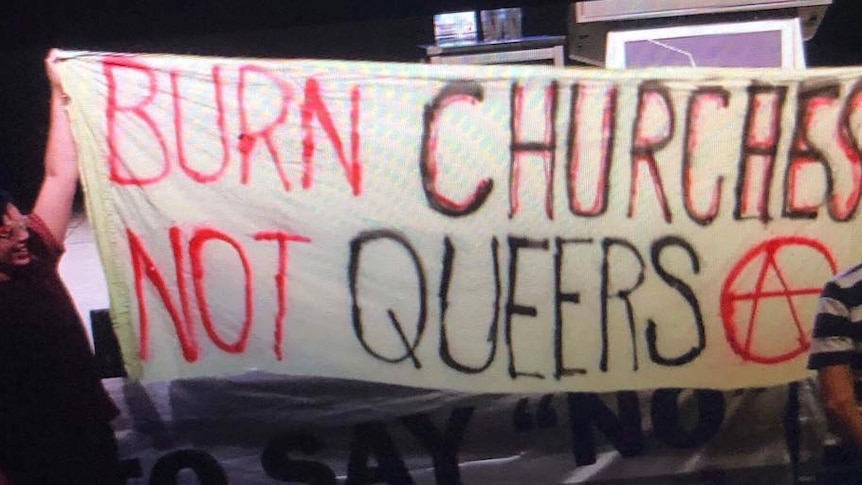 Protesters hold up a banner reading 'burn churches not queers'