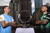 Jamie Maclaren and Josh Risdon look at each other with the A-League Men trophy in between them