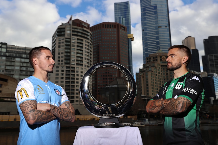 Jamie Maclaren and Josh Risdon look at each other with the A-League Men trophy in between them