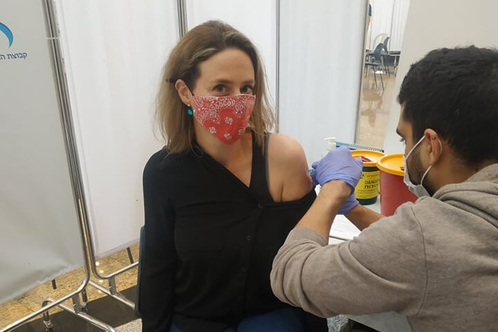 A woman in a red face mask receives an injection