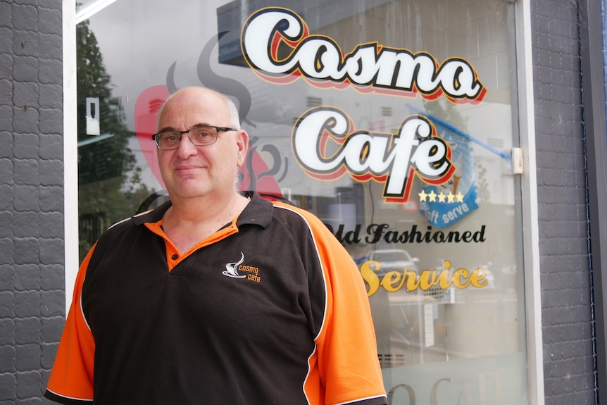 A man in a black and orange shirt outside a cafe window.
