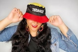A woman smiles and covers her face with a black, red and yellow hat.