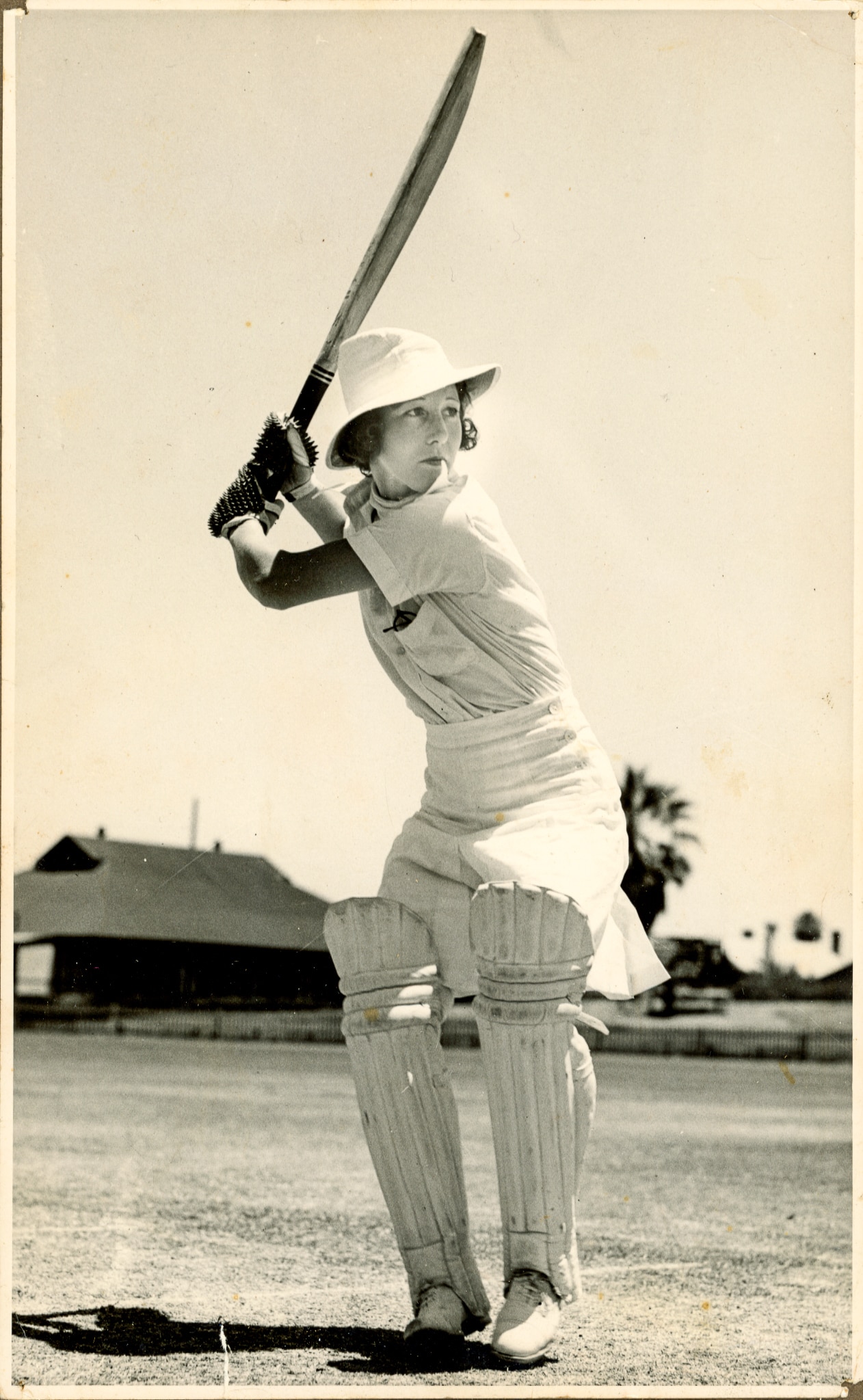 Hazel vestindo roupa branca de críquete com taco por cima do ombro depois de acertar uma bola